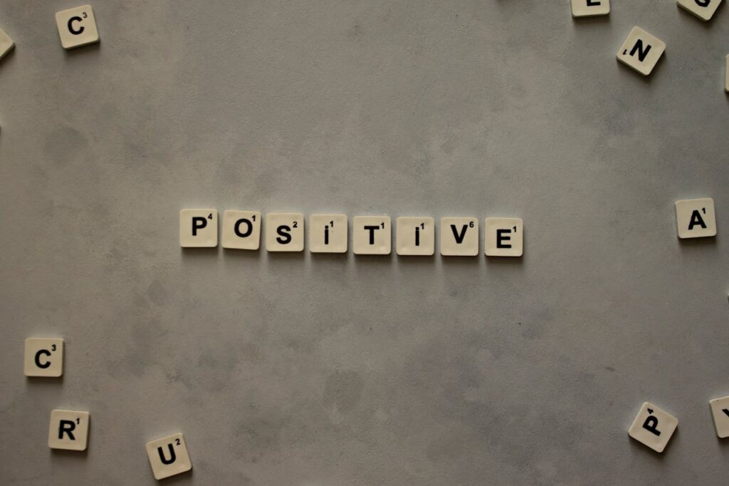 Scrabble tiles arranged to spell 'positive' on a gray textured surface, conveying optimism.